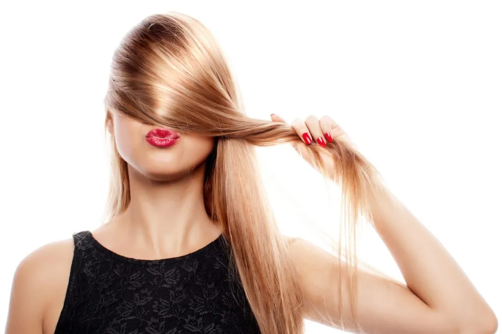 A woman holding her blonde hair over her eyes and nose Beautiful hair isolated on white.