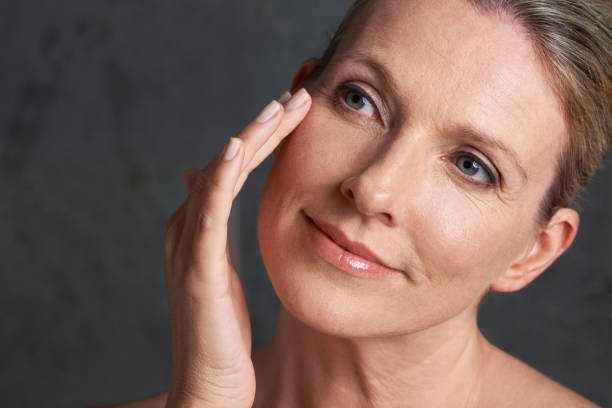 A mature woman with bare shoulders looking away against a gray background